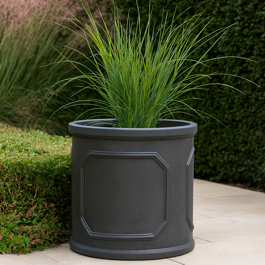 Gray planter with green grass-like plant against a green hedge background